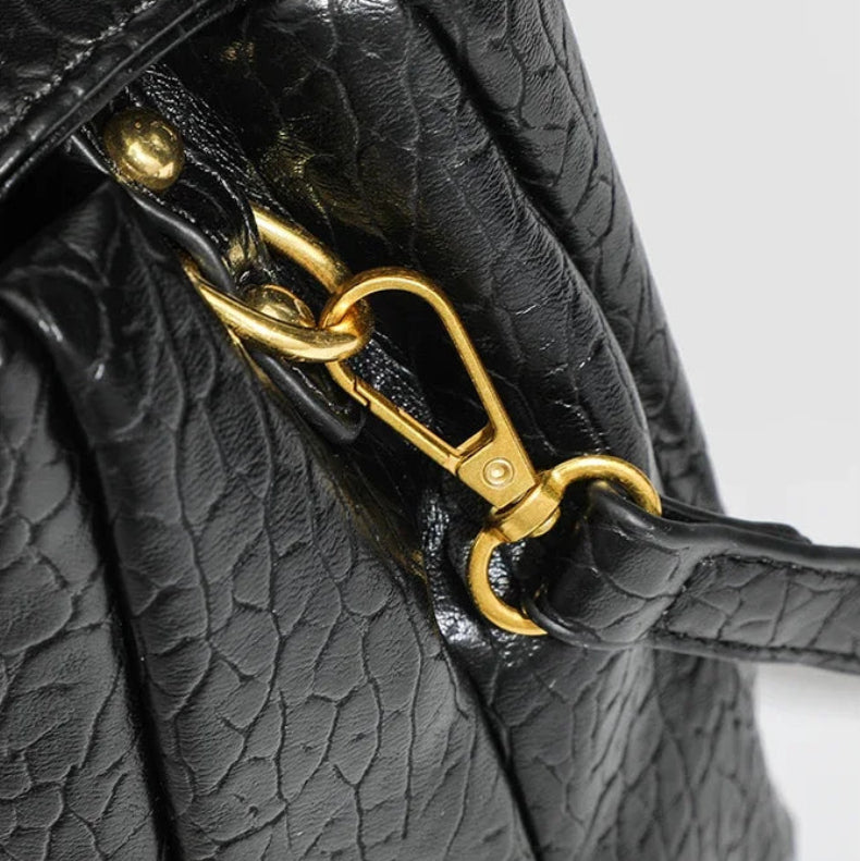 Black textured handbag with gold clasp on a light gray background