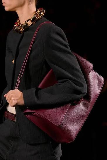 Person wearing a black outfit with a burgundy handbag on a dark background