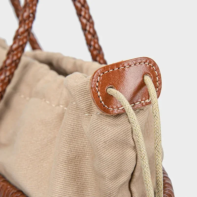 Close-up of a beige drawstring bag with brown leather pull tab on a light gray background