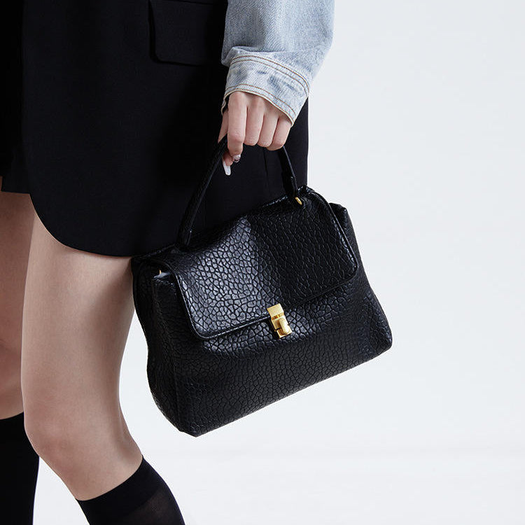 Person holding a black textured handbag on a white background