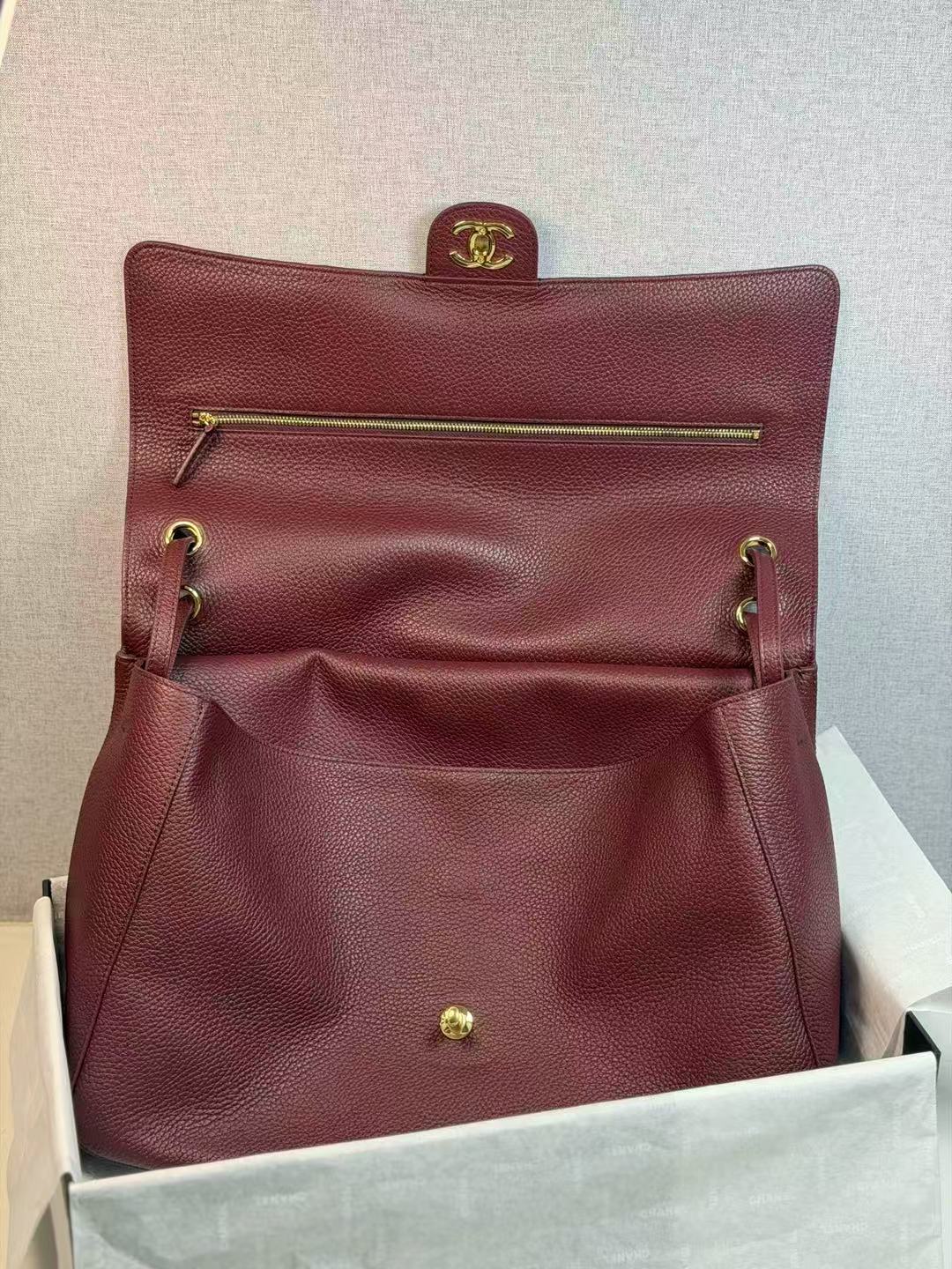 Burgundy leather handbag with gold accents in a box on a light gray background