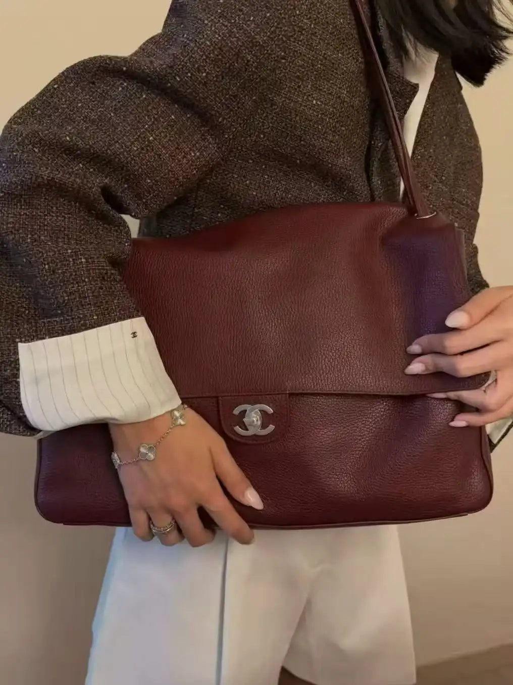 Person holding a maroon handbag with a visible brand logo against a neutral background