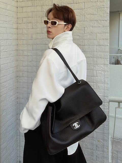Person wearing a white high-neck top and black Chanel handbag against a light stone wall.