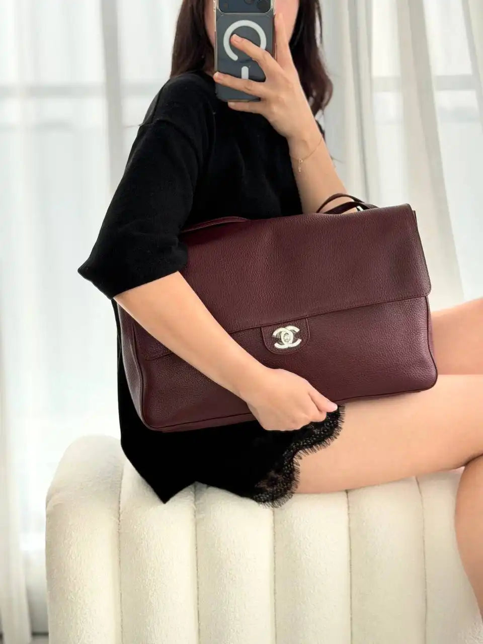 Person holding a brown leather handbag with a visible brand logo on a light-colored couch.