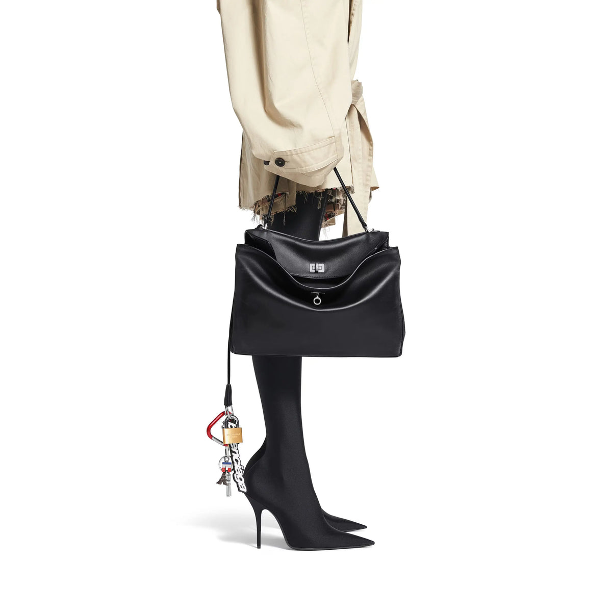 Black handbag with a tassel held by a person wearing black high heels on a white background