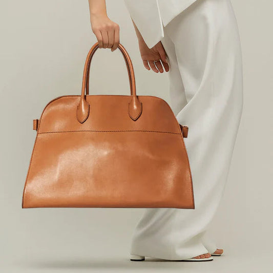 Person holding a brown leather handbag against a neutral background