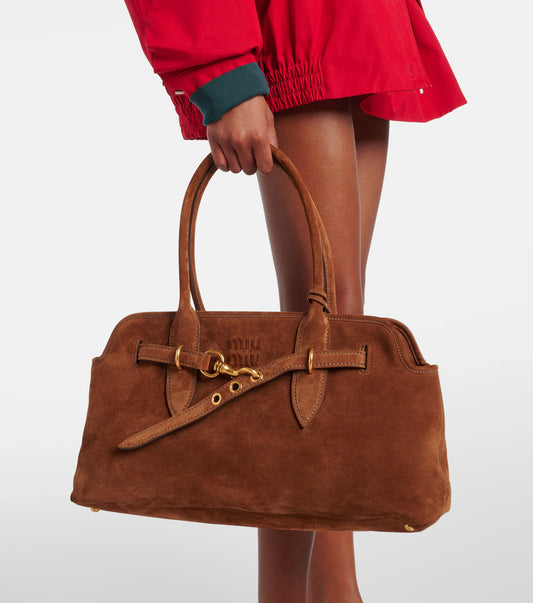 Brown suede handbag held by a person wearing a red jacket on a white background