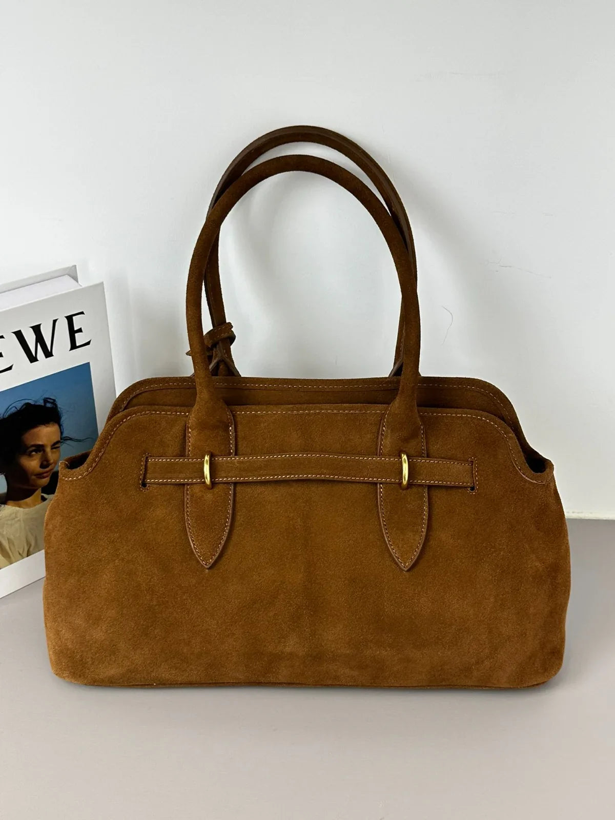 Brown handbag on a white surface with a blurred magazine in the background