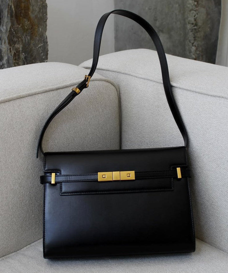 Black handbag with gold accents on a light gray surface with a stone wall background