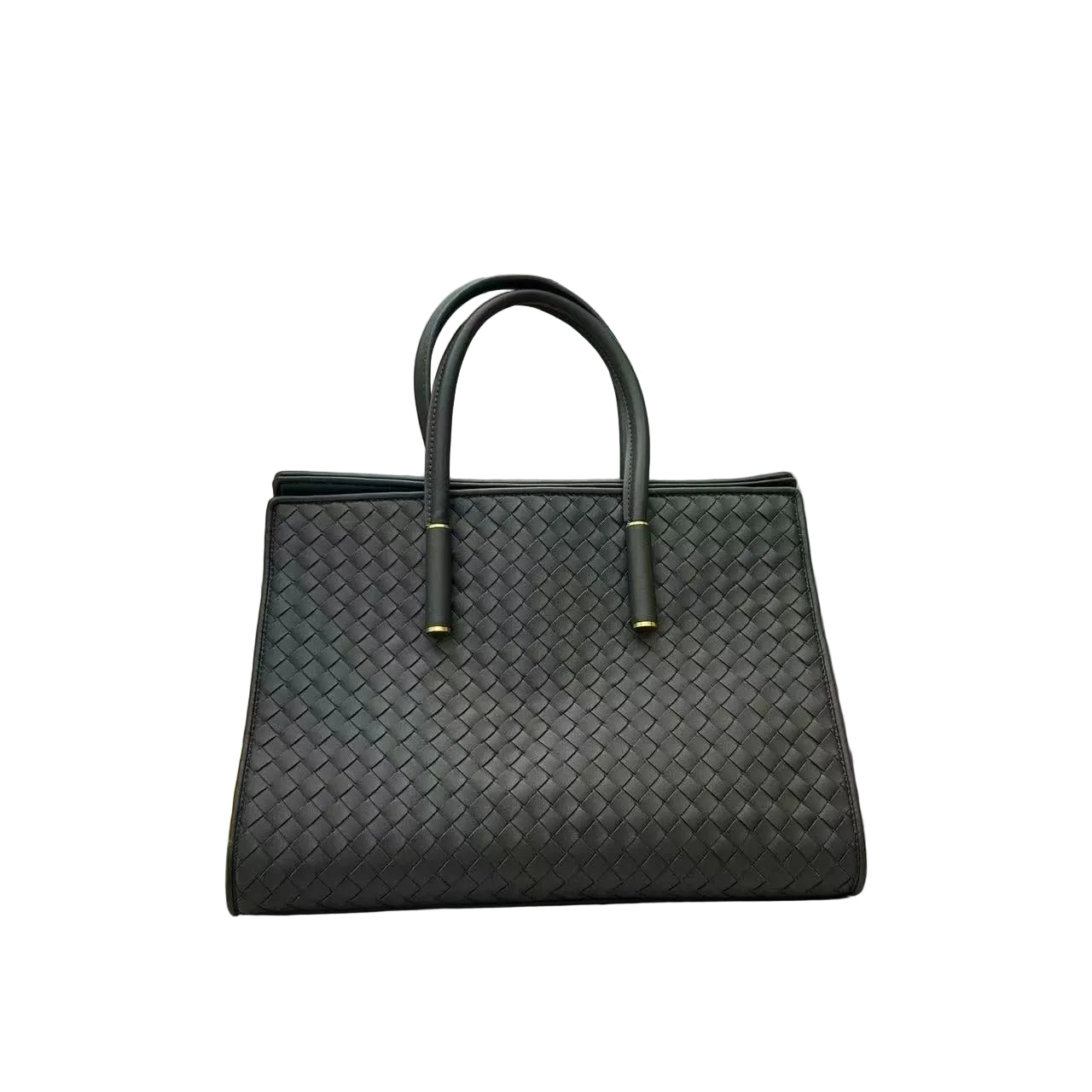 A black woven leather tote bag with double top handles and gold-tone hardware, resting on a white tiled floor in front of a white sofa.