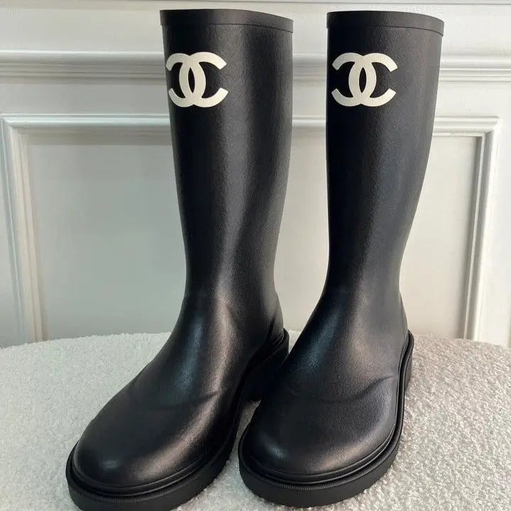 Pair of black rain boots with Chanel logo on a light gray surface.